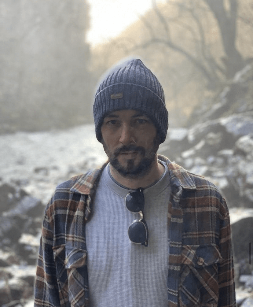 A traveler wearing a beanie and plaid shirt, standing near a serene outdoor backdrop, representing a journey with coeliac disease and gluten-free exploration